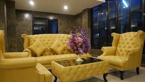 A room with a yellow tufted sofa set, a glass coffee table, and a vase of purple flowers. - Green Garden Place (Udon Thani)