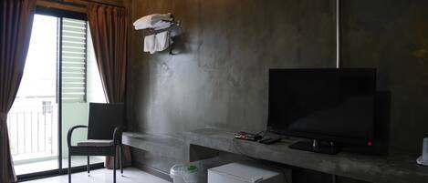 A hotel room with a bed, a chair, a TV, a small fridge, and a trash bin.
