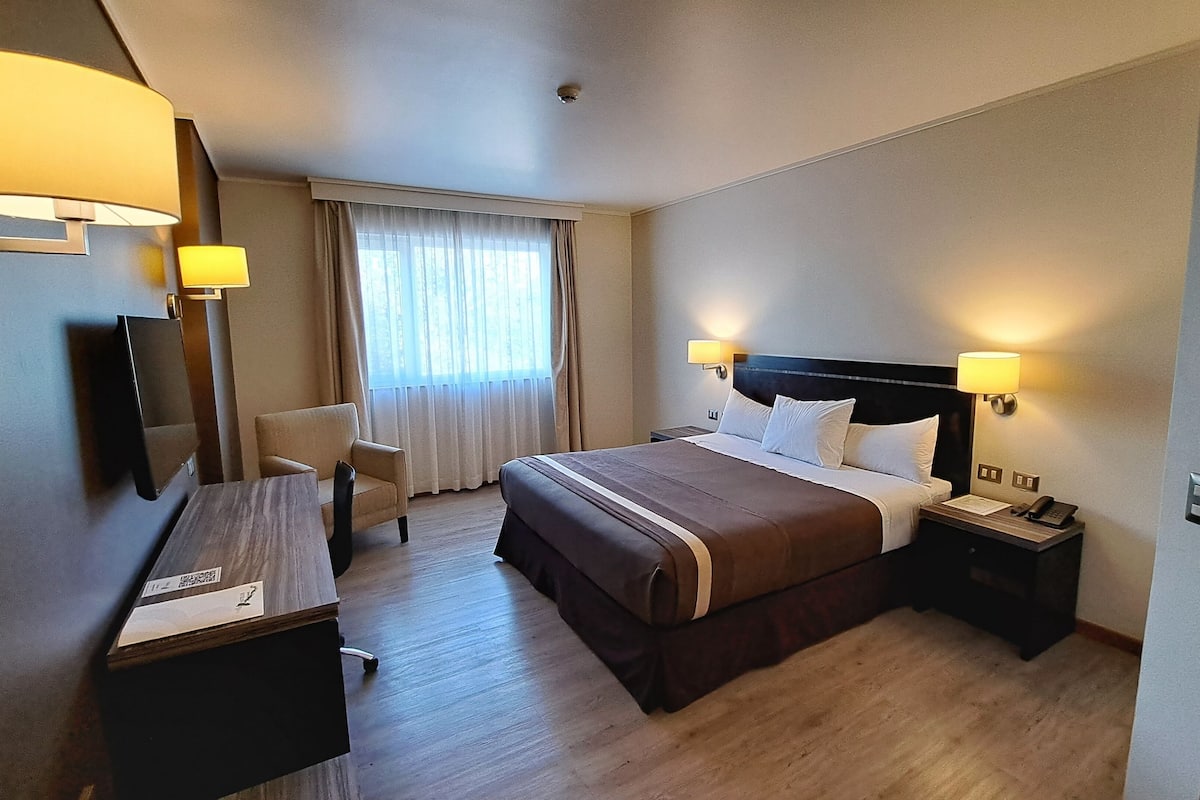 Een hotelkamer met een bed, nachtkastjes, een bureau, een stoel en een raam met gordijnen.