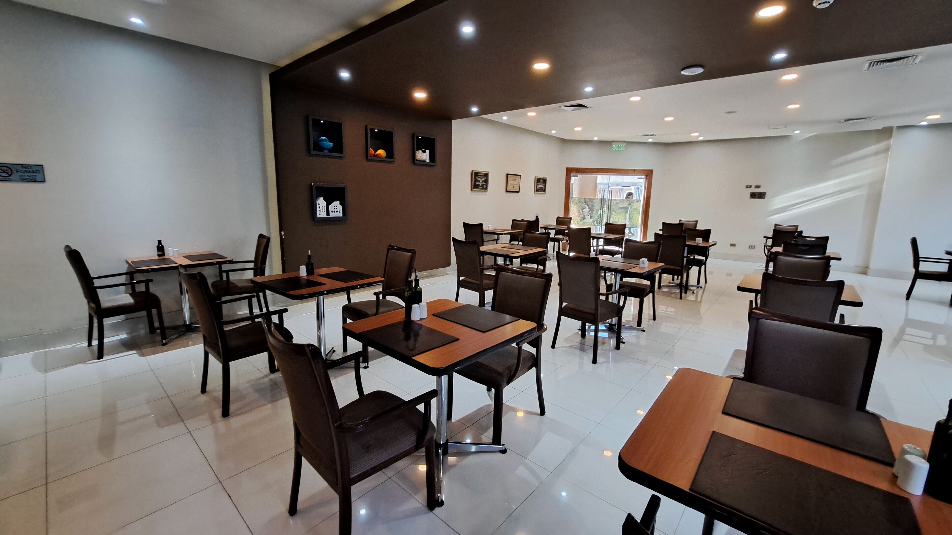 A spacious dining area with multiple tables and chairs, a clean tiled floor, and framed artwork on the walls.