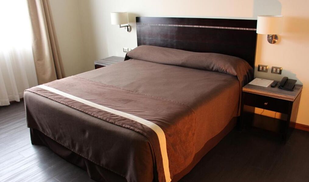 Una habitación de hotel con una cama grande, una mesita de noche con lámpara y un teléfono.