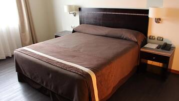 Una habitación de hotel con una cama grande, una mesita de noche con lámpara y un teléfono.