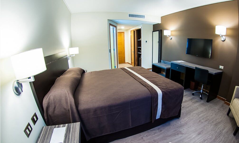 Une chambre d’hôtel avec un grand lit, un bureau avec une chaise, une télévision et une armoire.