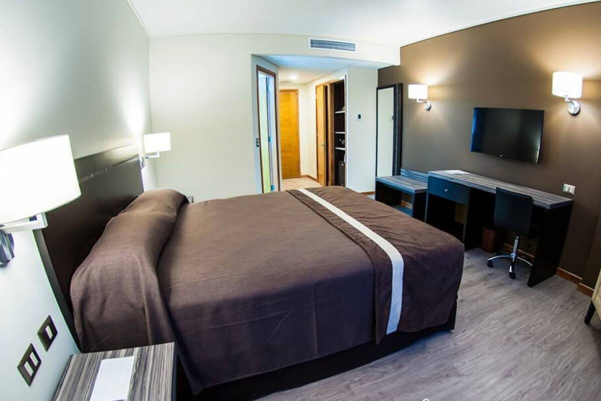 Een hotelkamer met een groot bed, een bureau met stoel, een televisie en een kledingkast.