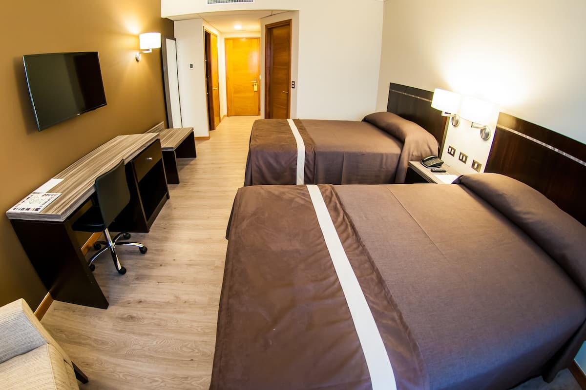 Een hotelkamer met twee bedden, een bureau, een stoel, een televisie en een lamp.