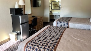 A hotel room with two beds, a refrigerator, a desk with a chair, a mirror, and a bathroom visible through an open door. - Economy Inn (McCook)