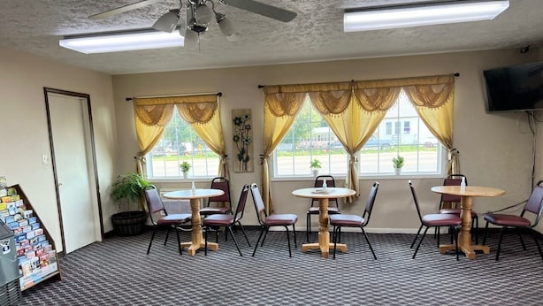 A conference room with four tables and chairs, large windows with curtains, a ceiling fan, and a wall-mounted TV. - Economy Inn (McCook)
