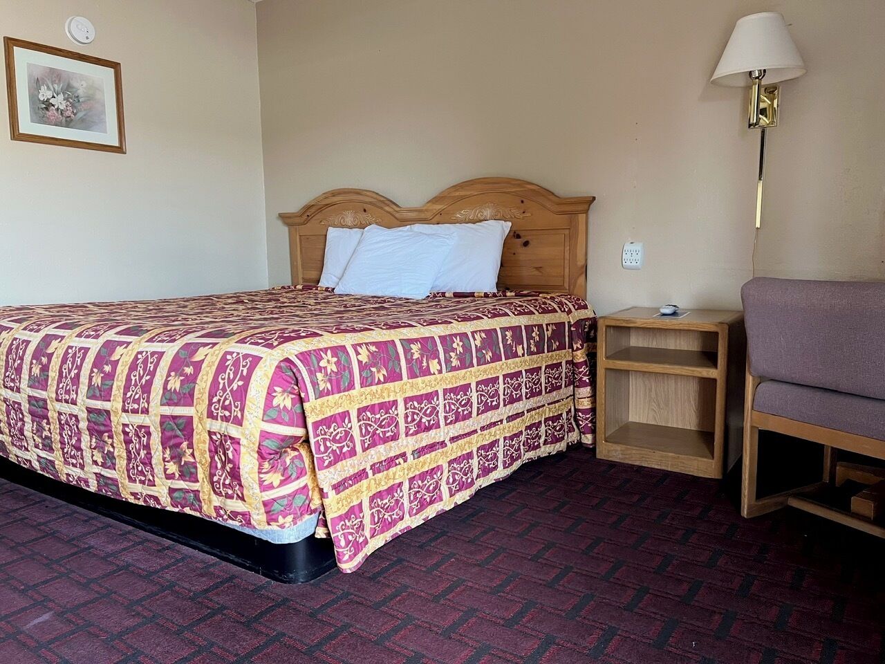 Una habitación de hotel con cama, mesita de noche, lámpara y silla.
