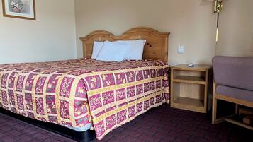 Una habitación de hotel con cama, mesita de noche, lámpara y silla.