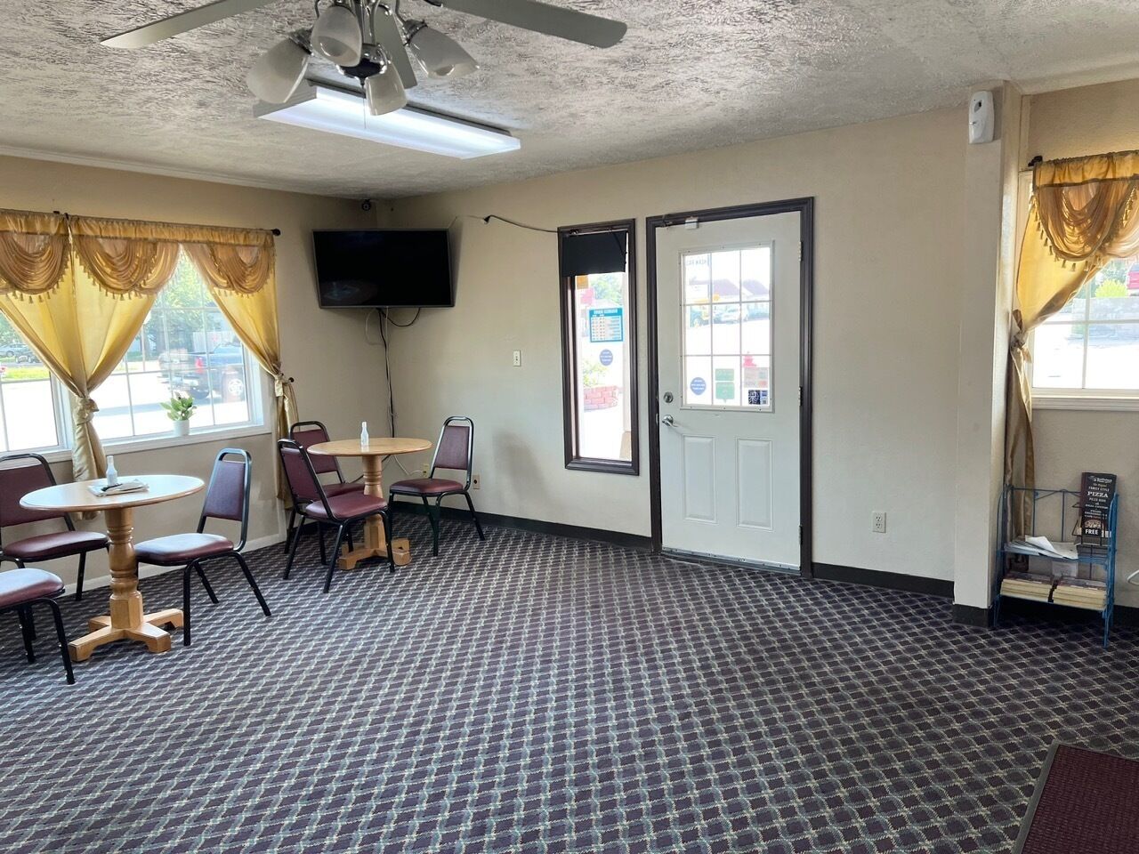 A room with a patterned carpet, a ceiling fan, a flat-screen TV mounted on the wall, and a door with a window.