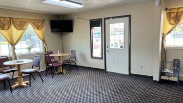 A room with a patterned carpet, a ceiling fan, a flat-screen TV mounted on the wall, and a door with a window.