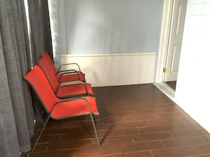 Una habitación con suelo de madera, una puerta blanca y una silla roja frente a una cortina gris.