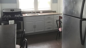 A kitchen with white cabinets, a stainless steel refrigerator, a stove, and a window with blinds. - HC-55 Beach Haus (Seaside Heights)