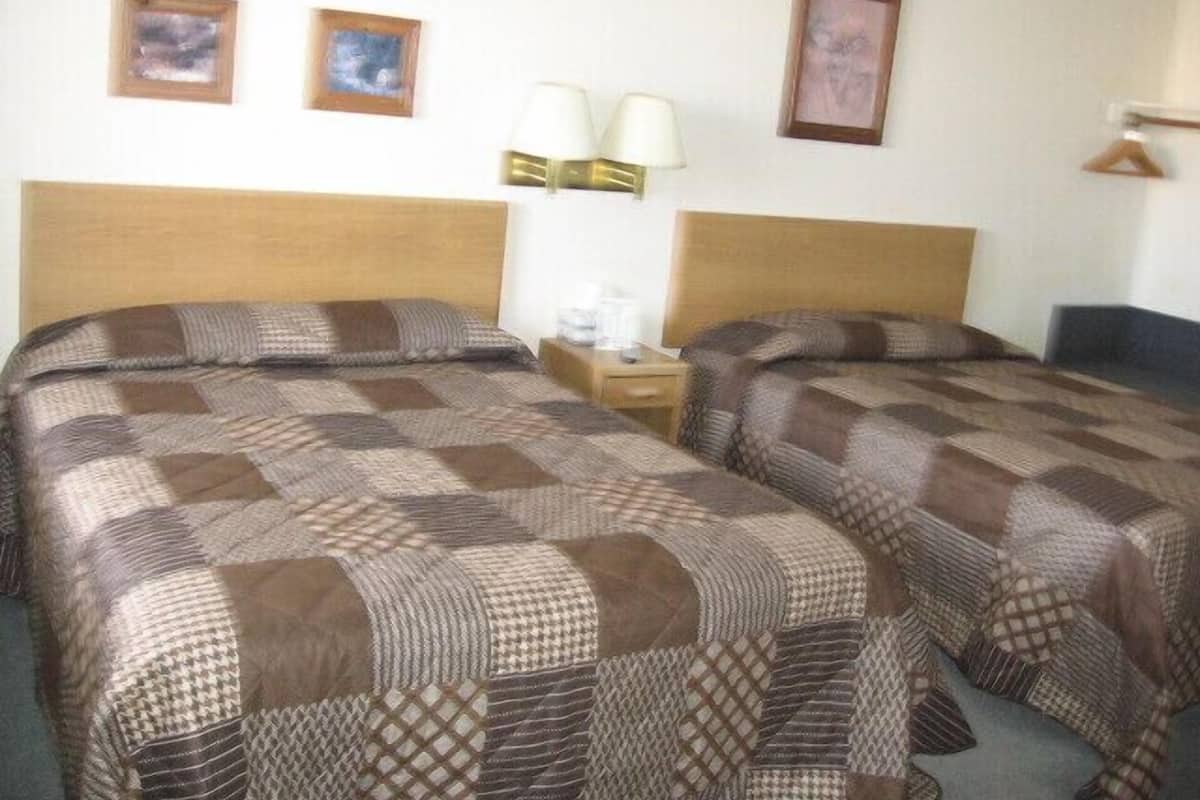 A double room with two beds, a nightstand with a lamp, and wall-mounted pictures.