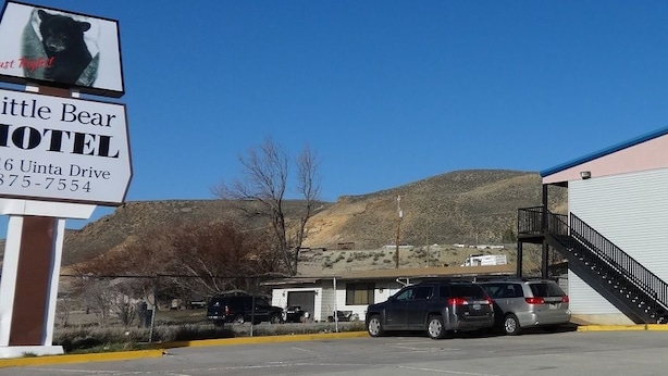 A motel with a large sign, a staircase, and a parking lot with cars. - Little Bear Motel (Green River)