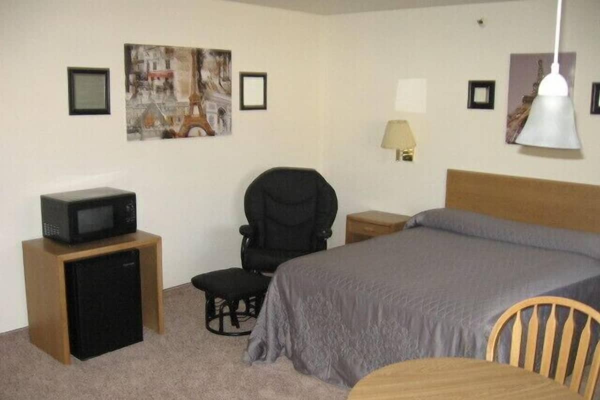 A hotel room with a bed, a desk with a computer, a chair, a small table, and a lamp.