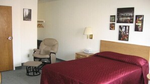 A hotel room with a large bed, a chair, a nightstand, and a lamp. - Little Bear Motel (Green River)