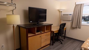 Habitación de hotel con escritorio, silla, televisión, lámpara, aire acondicionado y ventana con cortinas.