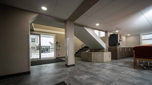 Un vestíbulo espacioso con diseño moderno, que presenta una pared de acento de piedra, una escalera y una zona de estar con un sillón rojo.
