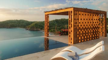 A wooden pergola with a poolside lounge chair and a towel.
