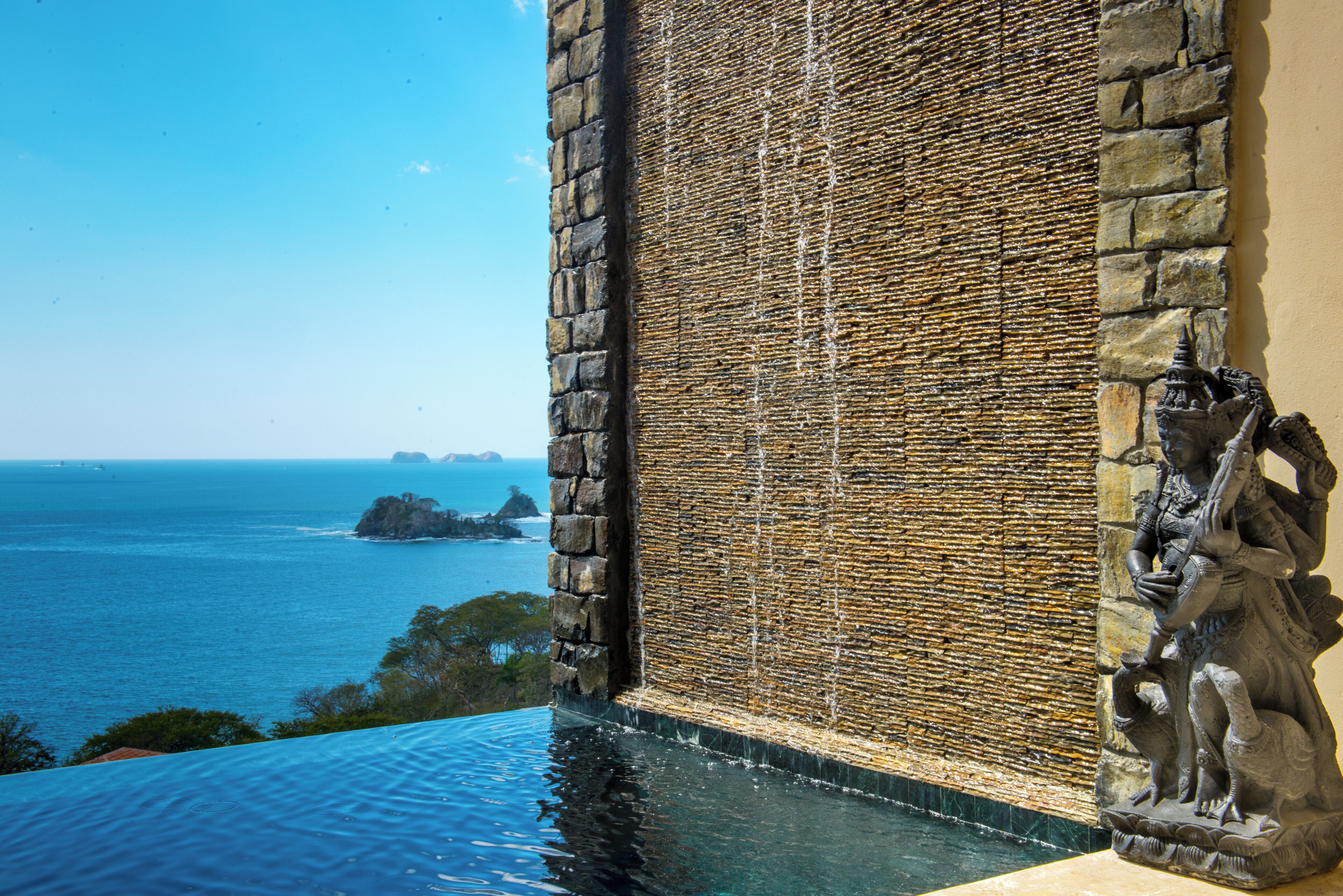 A stone wall with a water feature, a view of the ocean, and a statue.