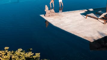 Una pareja está de pie en la terraza de una piscina, con vista a un mar tranquilo y una isla distante.