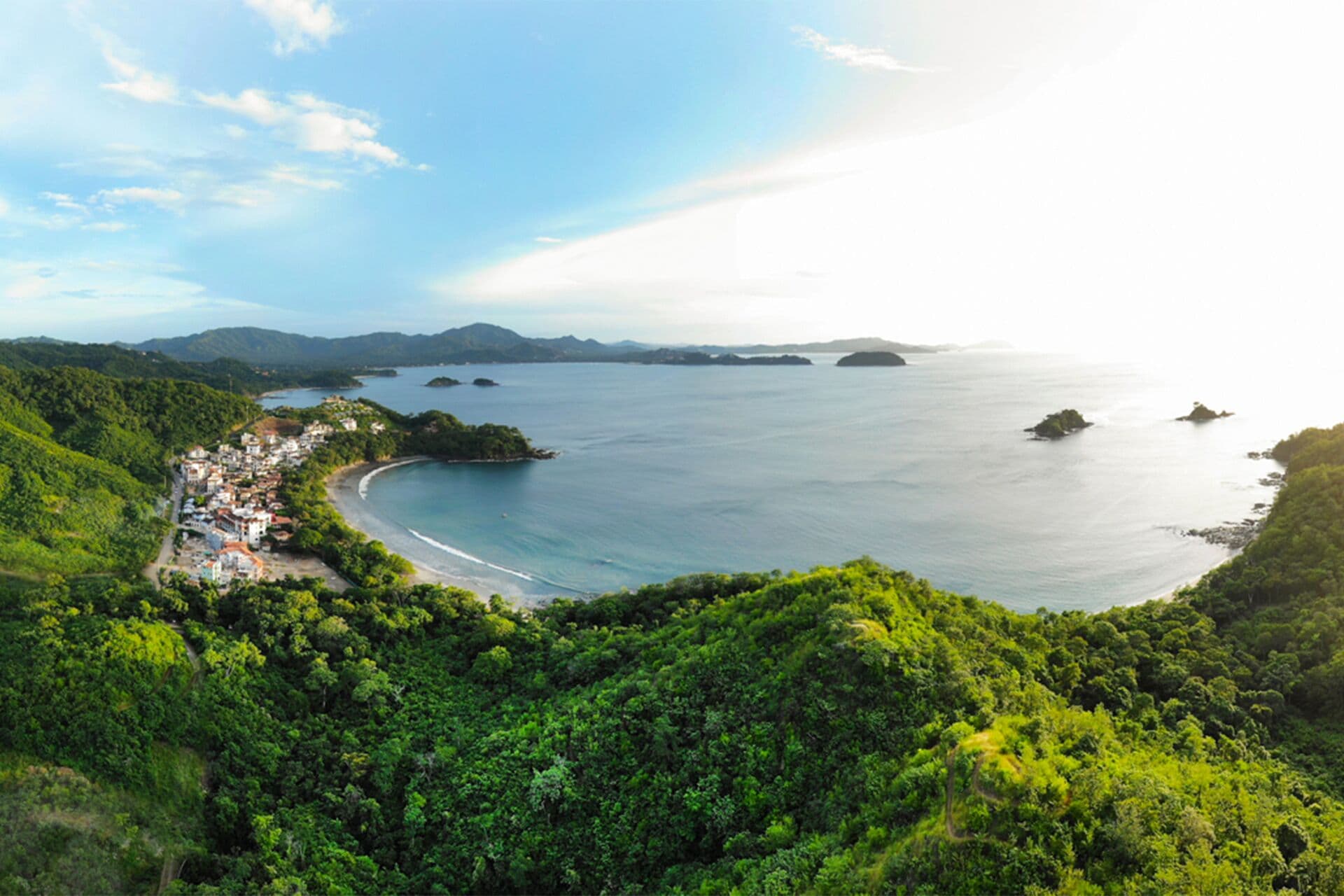 A coastal town with a beach, surrounded by lush greenery and hills.