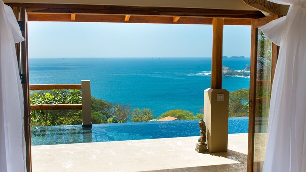 A room with a view of the ocean, a patterned rug, and a statue.