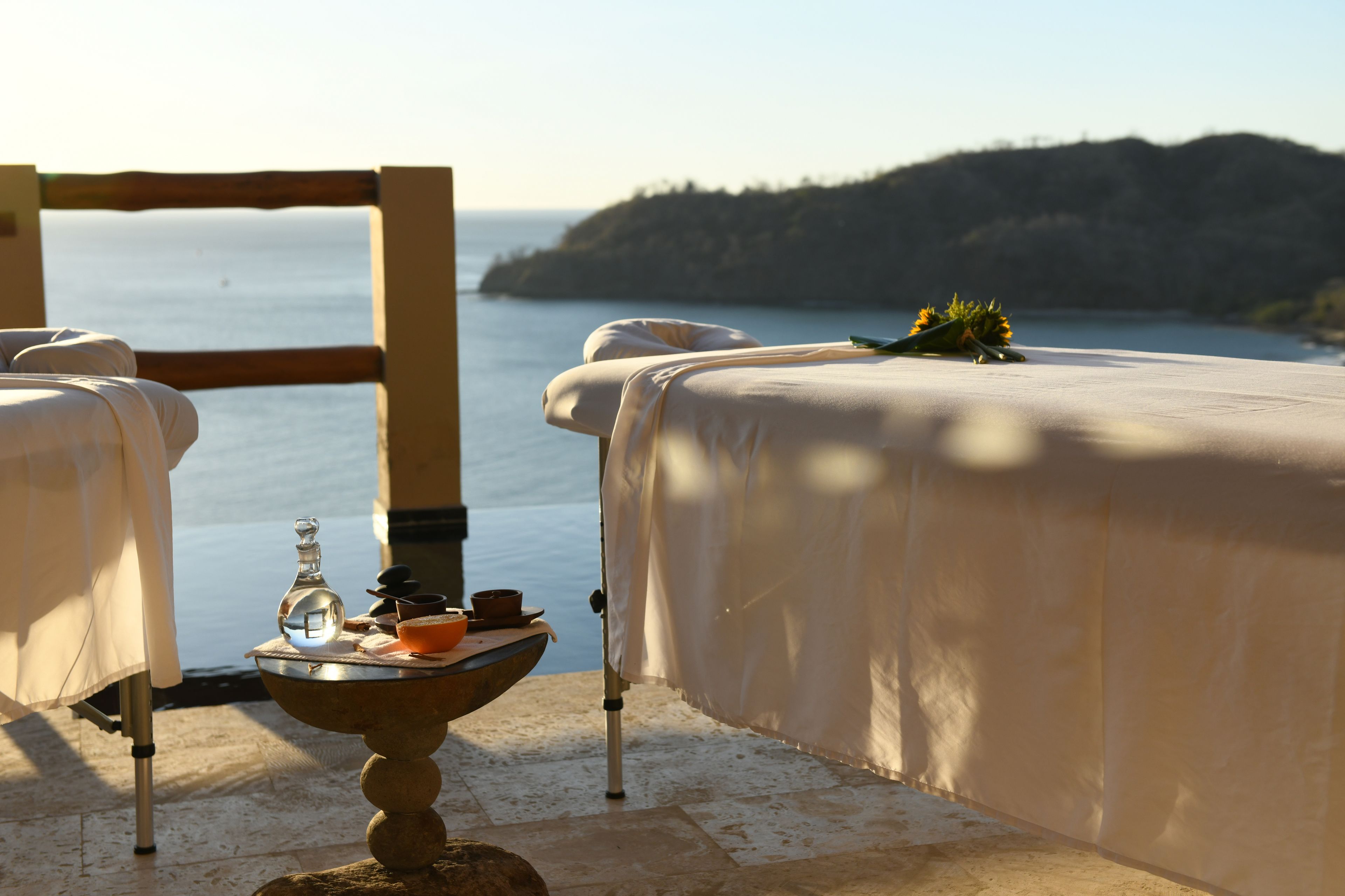 Un espacio exterior tranquilo con vistas al mar, una mesa con una botella y un cuenco, y una silla con cojín.