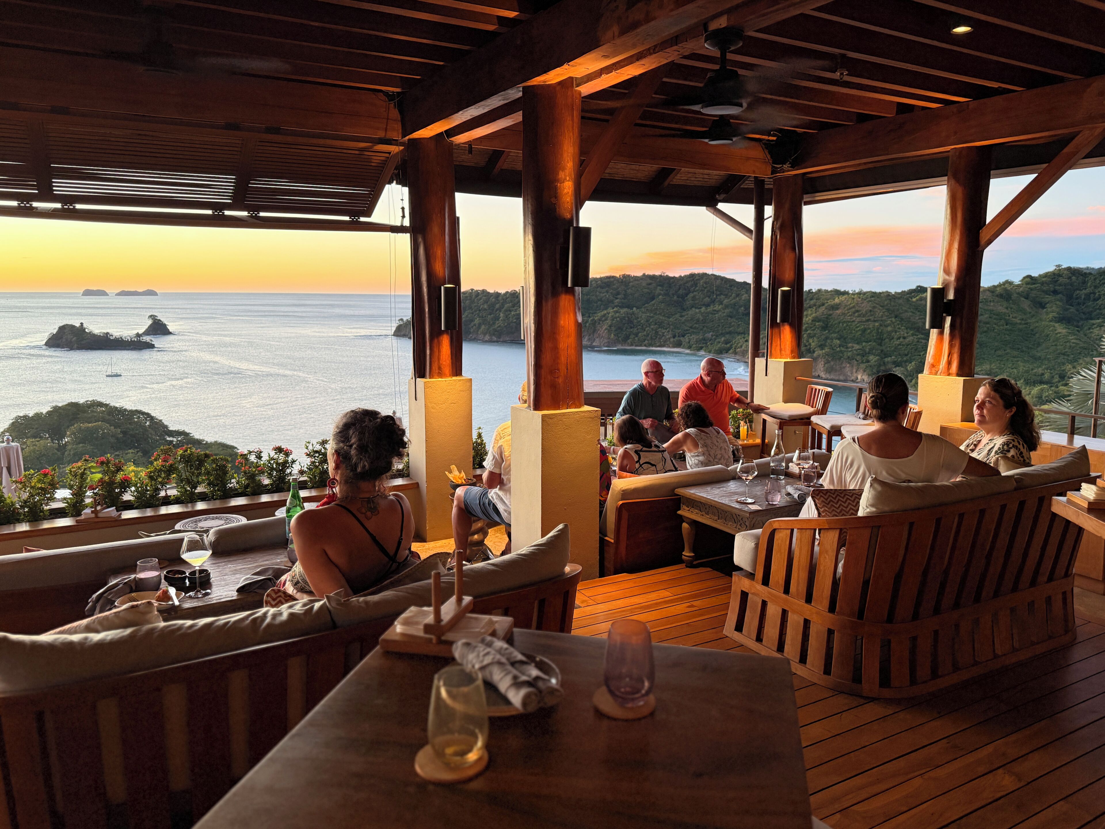 Un espace extérieur aménagé avec des meubles en bois, des tables et une vue sur la mer et les îles.