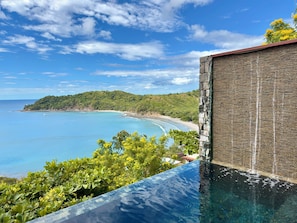 A clear view of a coastal landscape with a swimming pool, a beach, and a mountainous backdrop.