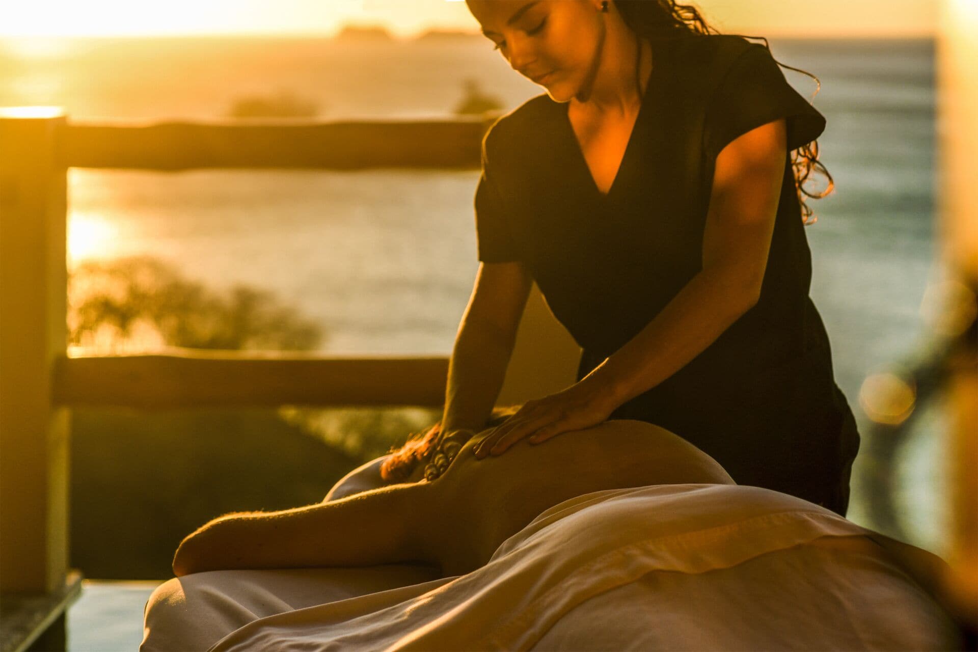 A person receiving a massage on a wooden deck with a view of the ocean.