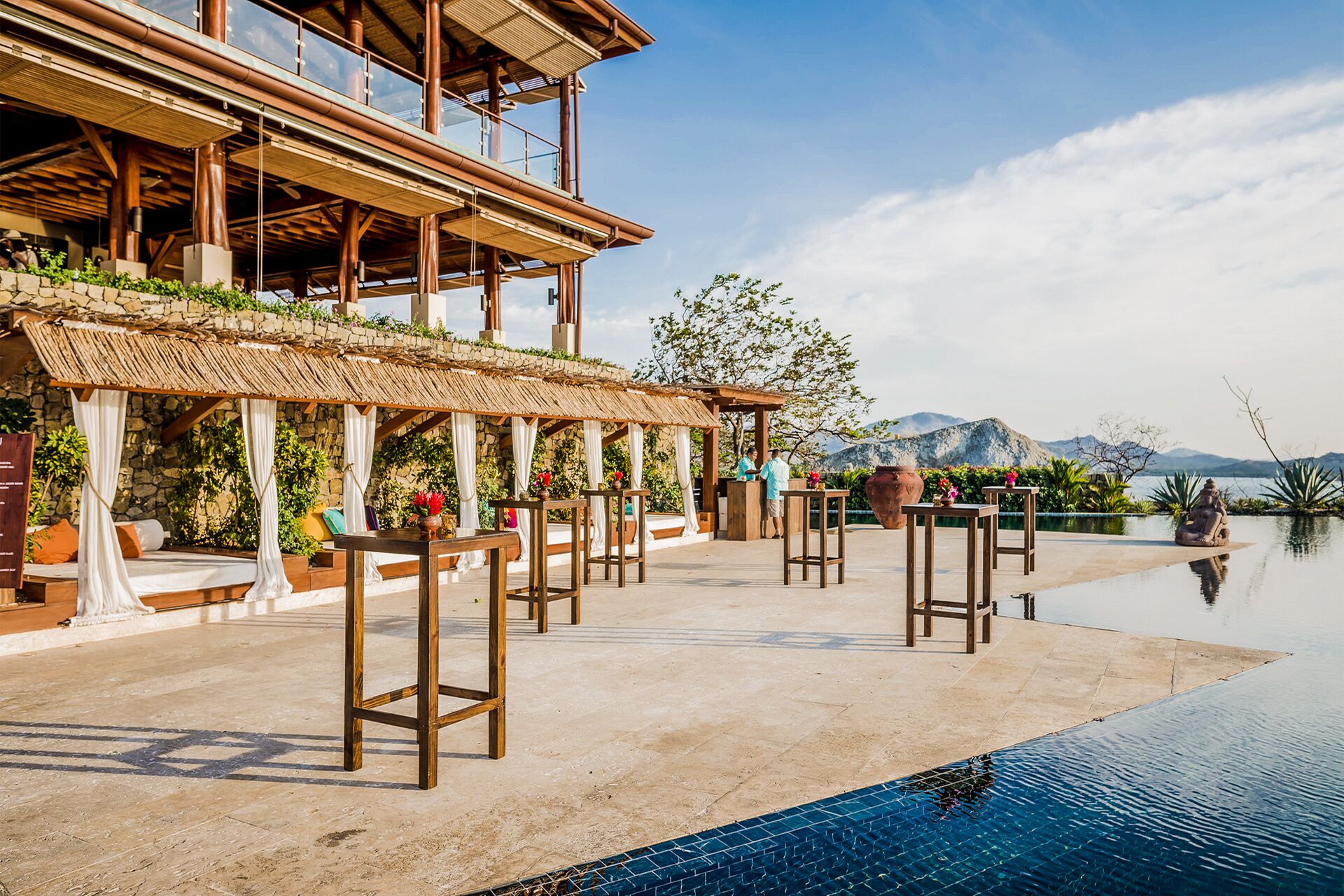 Un espace aménagé au bord de la piscine, avec des tabourets de bar, un coin salon abrité et une vue sur les montagnes.