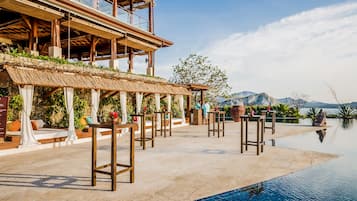 A poolside area with bar stools, a covered seating area, and a view of mountains.