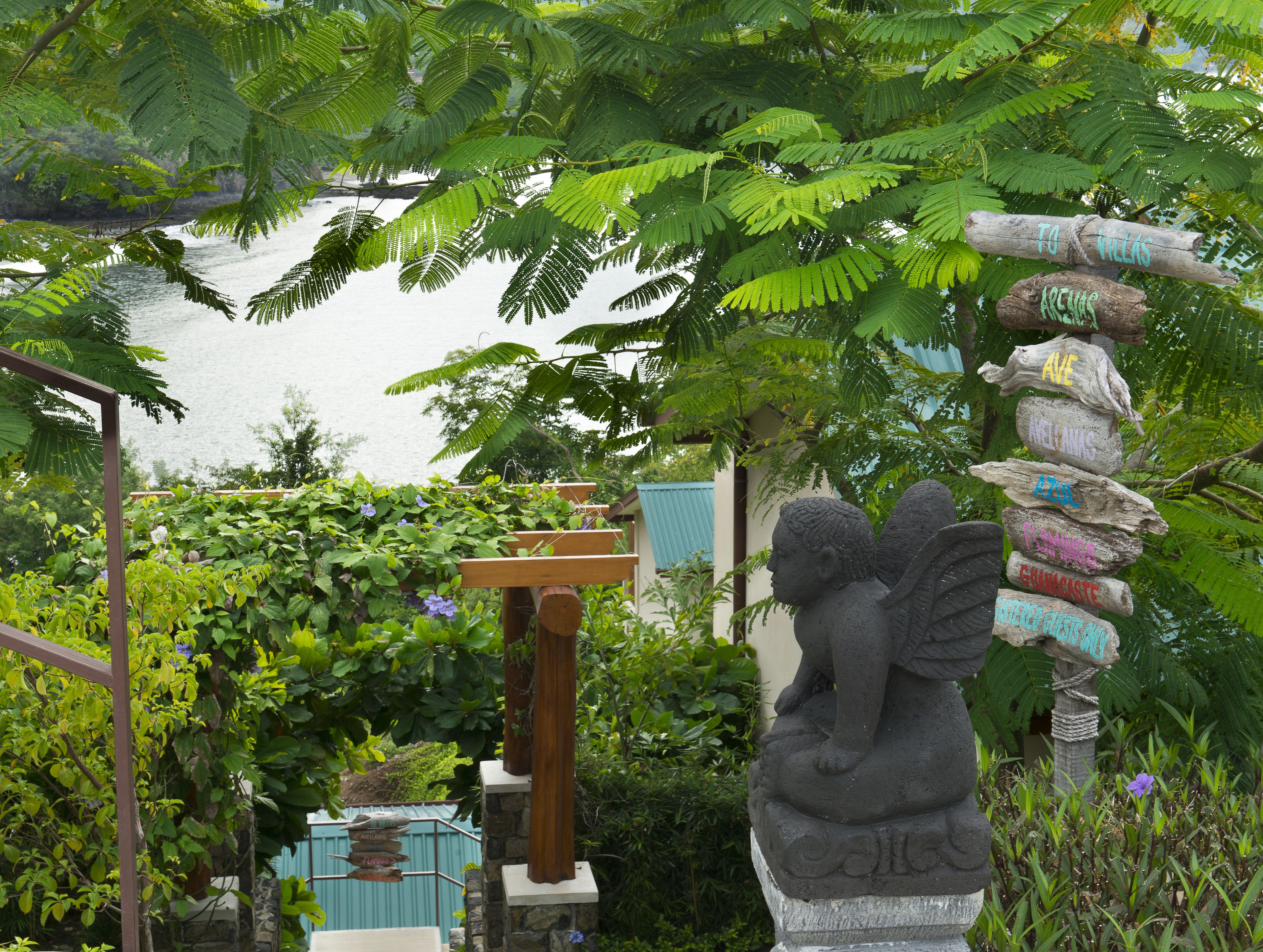 Un jardín con una estatua de piedra de un ángel sosteniendo un cartel con varios nombres.
