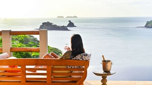 A wooden bench with a person sitting, overlooking a calm sea with distant islands.