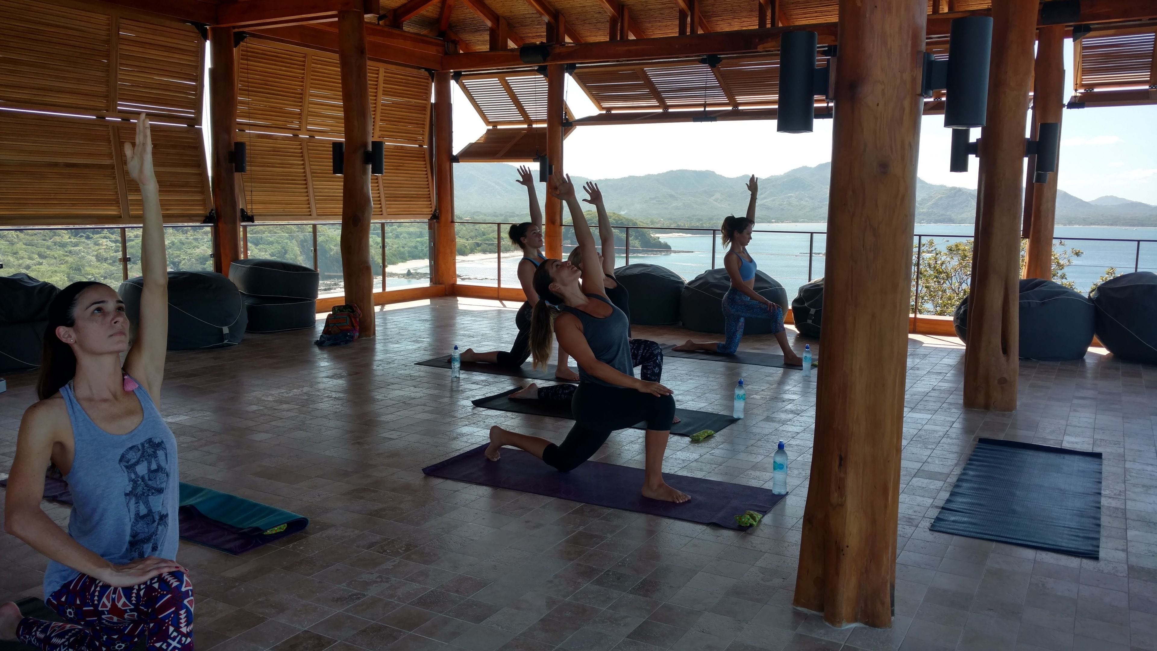 Aula de yoga numa sala ampla com grandes janelas e vista panorâmica para montanhas.