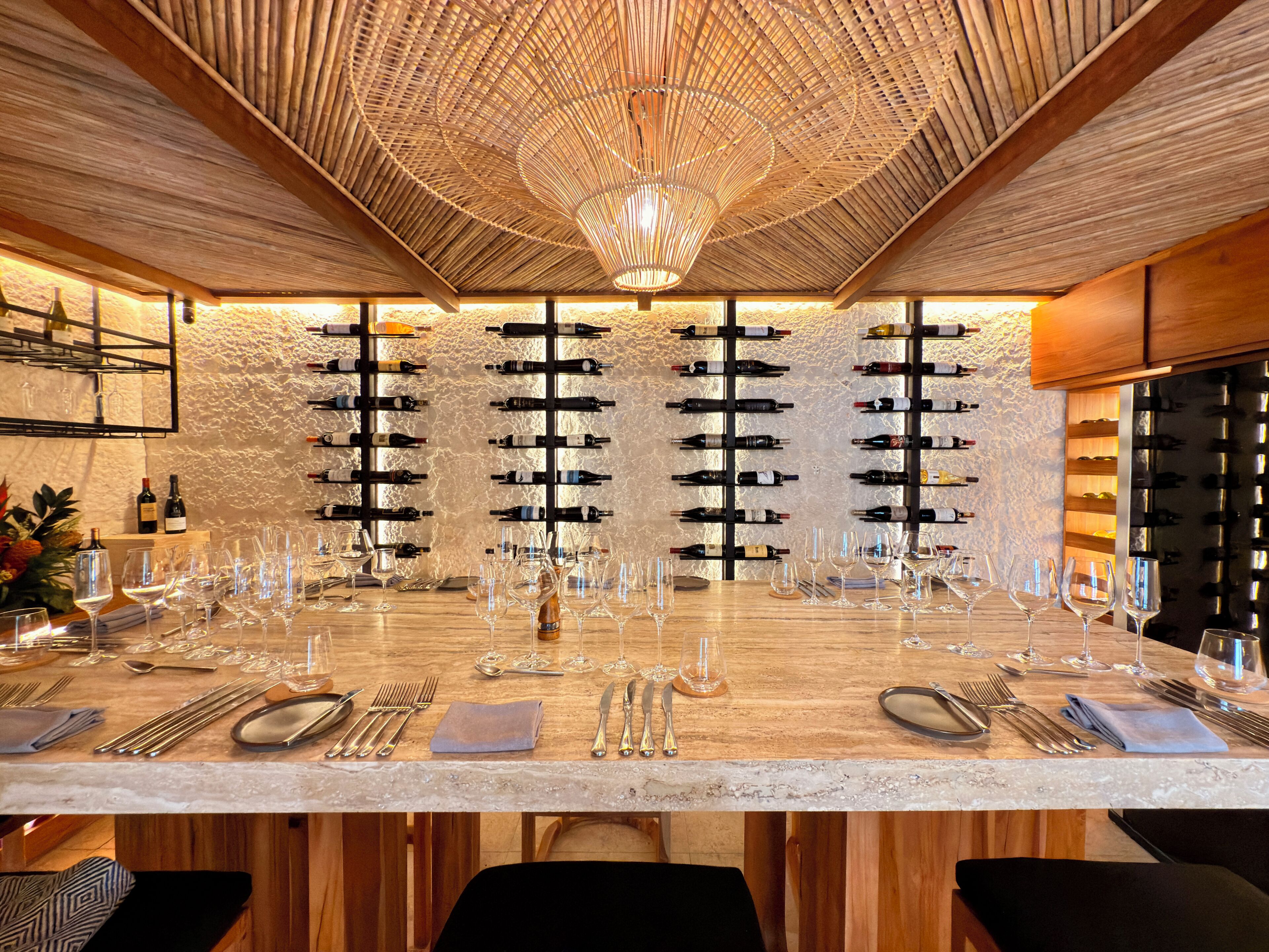 A restaurant with a long table set for dining, wine racks on the wall, and a wooden ceiling.