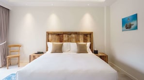 Habitación de hotel con una cama grande, cabecero de madera, dos mesitas de noche, una silla y un cuadro en la pared.