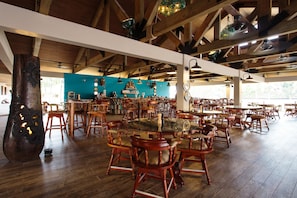 Un restaurante amplio con mesas y sillas de madera, una pared azul y un gran pilar de madera.
