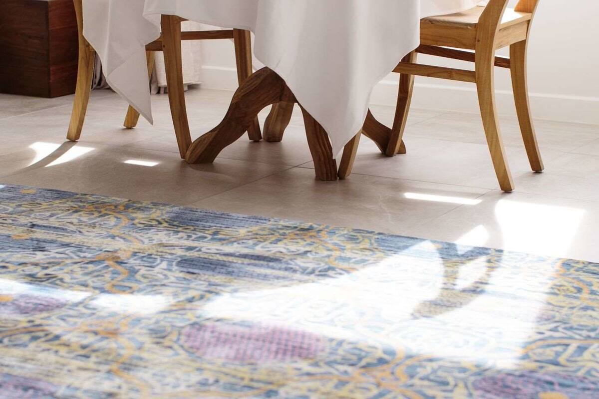 Um quarto com um tapete estampado, cadeiras de madeira e uma mesa com toalha branca.