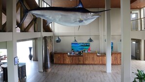 A spacious lobby with a large wooden reception desk, a hanging fish sculpture, and a large window providing natural light. - Cove Resort Palau (Malakal Island)