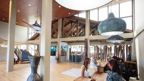 A spacious lobby with high ceilings, a staircase, and a large hanging light fixture. - Cove Resort Palau (Malakal Island)
