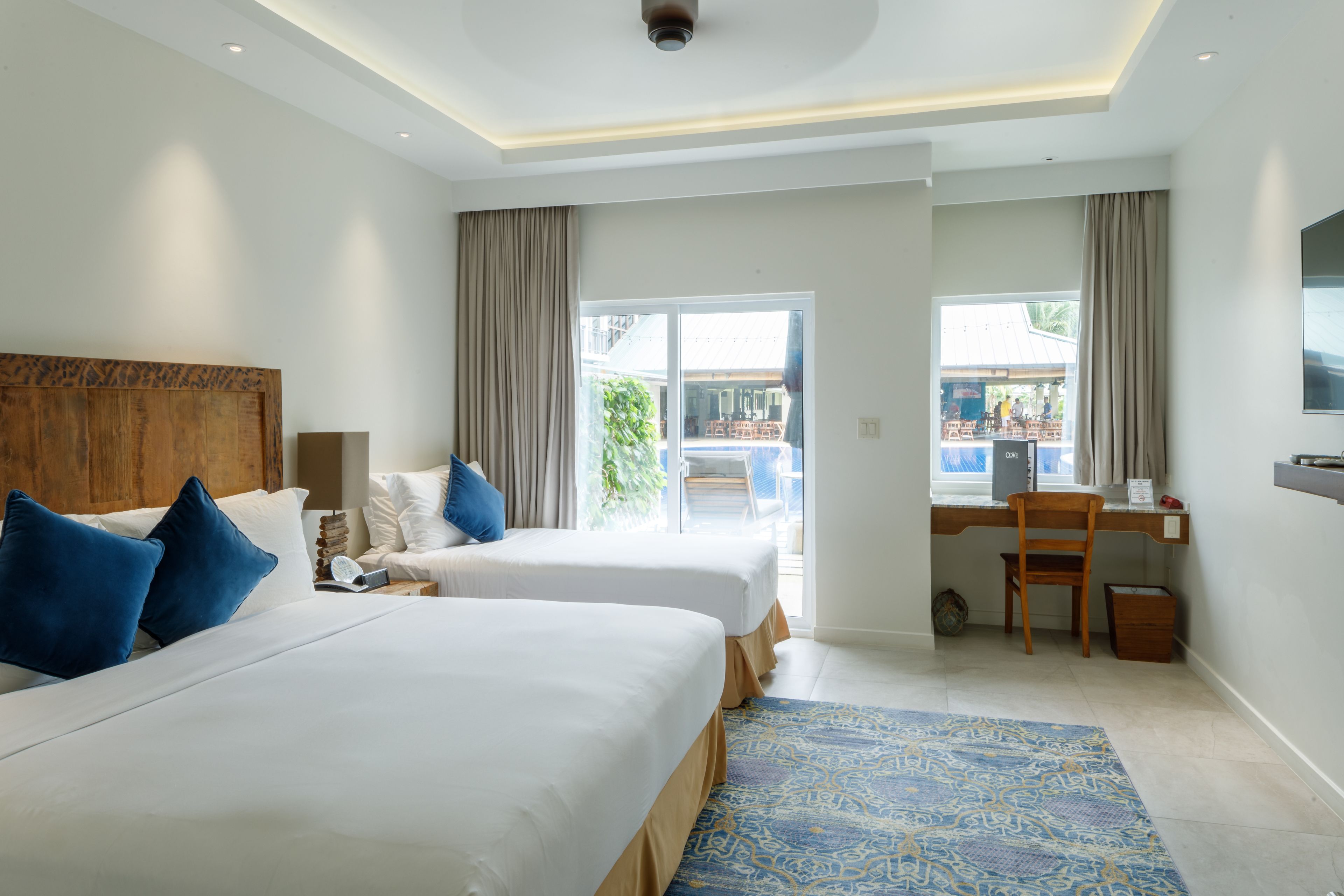 Een hotelkamer met twee bedden, een bureau en uitzicht op buiten.
