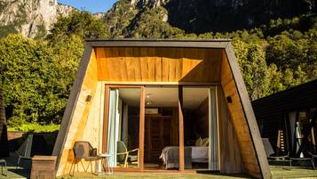Una cabaña tipo A de madera con puerta corrediza de vidrio, una cama y un área de descanso con sillas.
