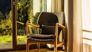 A room with a wooden chair by a large window, a wooden floor, and a view of a mountainous landscape. - Hotel Raudal (Palena)