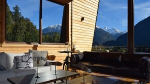 A modern living room with a wooden floor, a black leather sofa, a white sofa, and a dining table with a bowl of food. - Hotel Raudal (Palena)