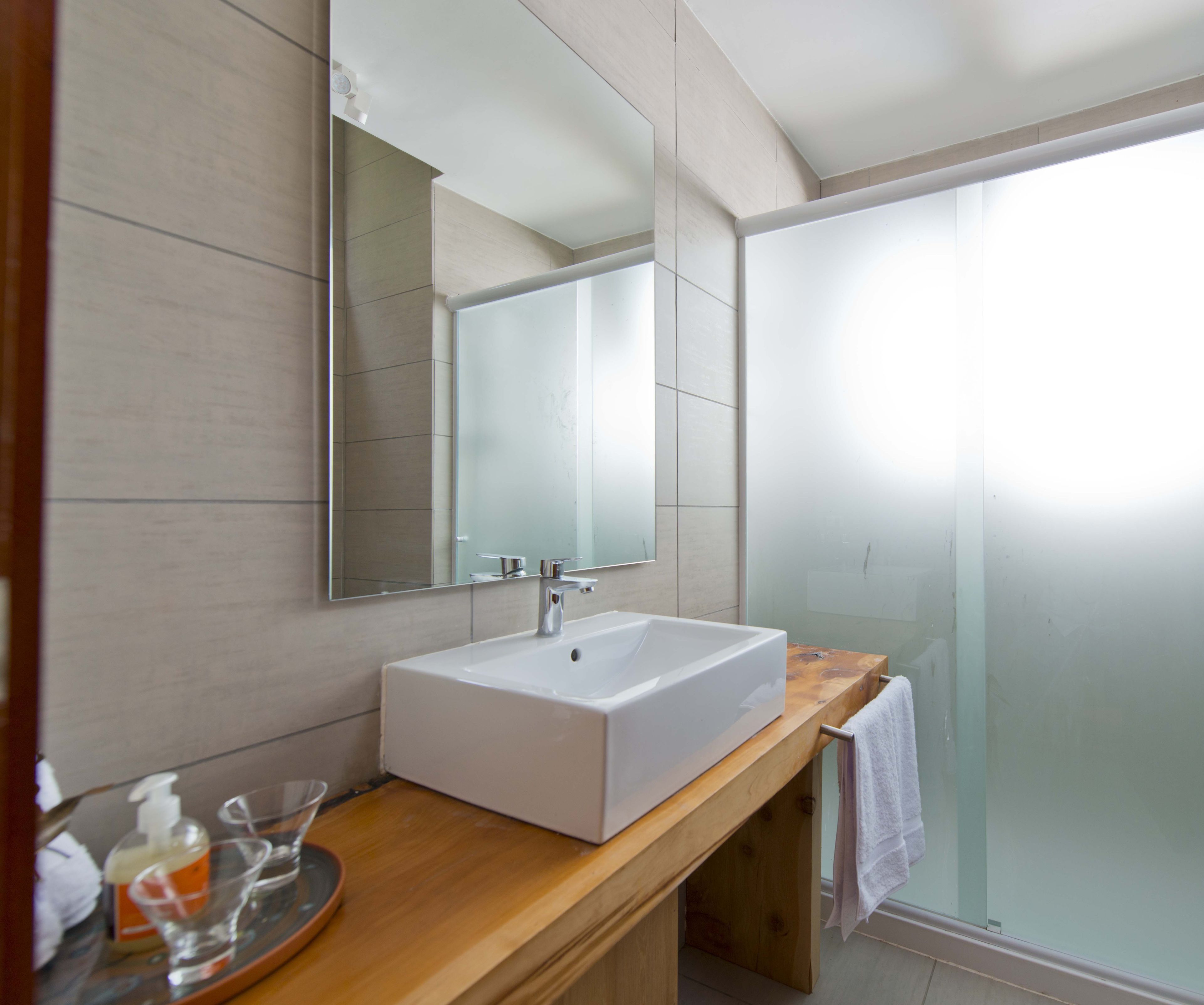 Un baño moderno con un lavabo blanco, un espejo grande y una cabina de ducha de vidrio.