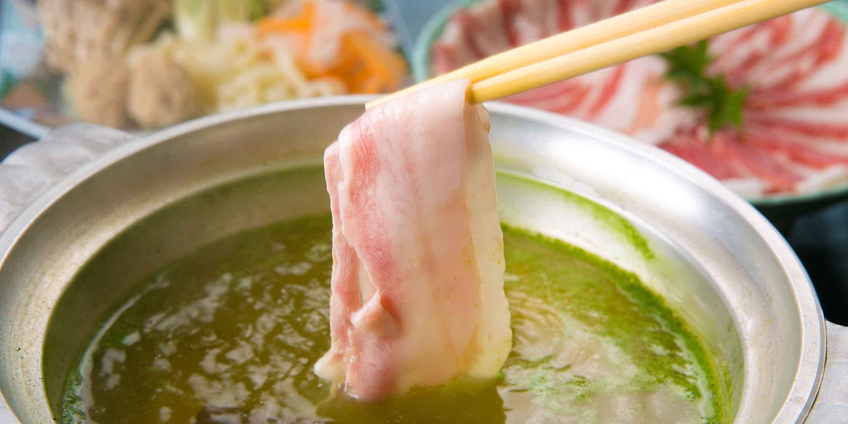 A hot pot with a piece of meat being held by chopsticks.