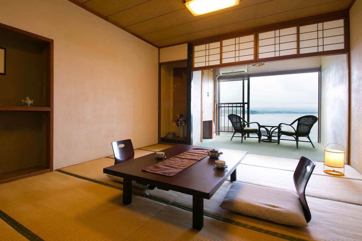 Une pièce de style japonais traditionnel, avec un sol recouvert de tatamis, une petite table sur laquelle est disposé un service à thé, et une vue sur la mer grâce à de grandes fenêtres.